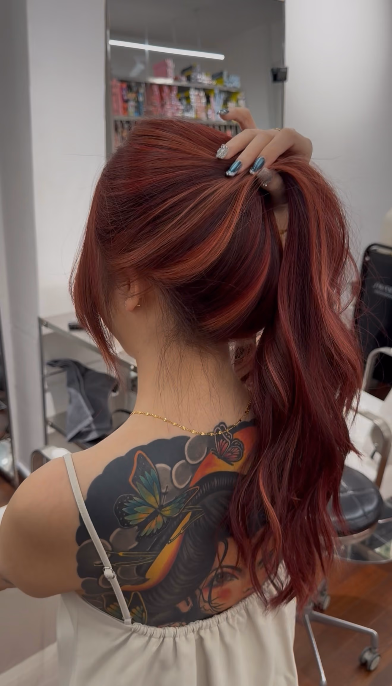 Woman with long red hair tied up and colorful back tattoo showing butterflies and a face.