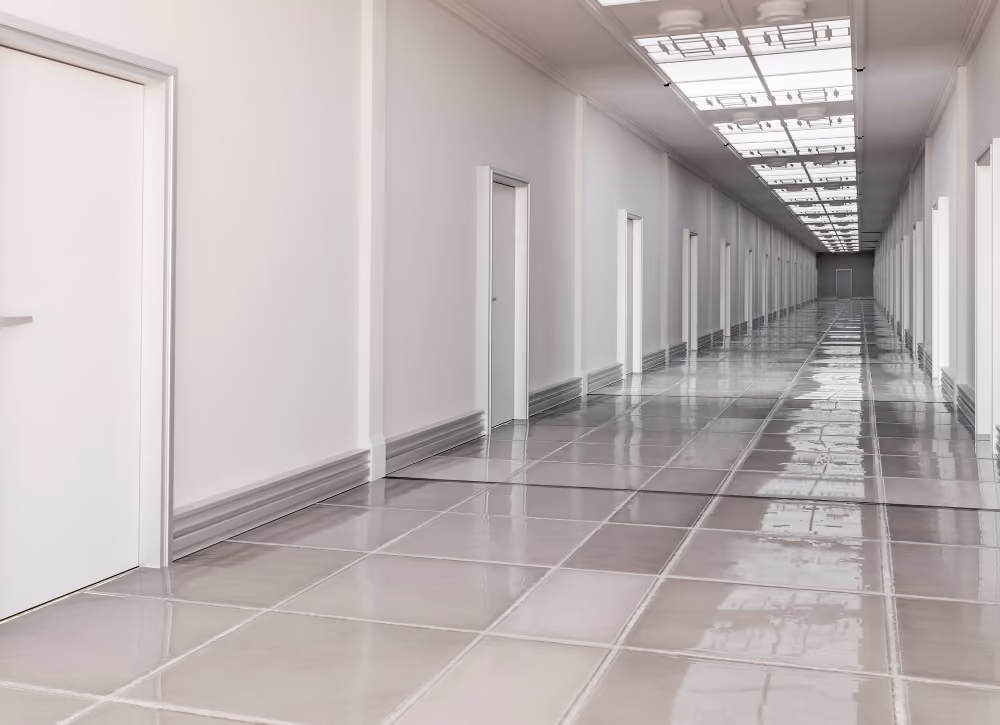 Long, empty hallway lined with white doors and reflective tiled floors under ceiling lights.