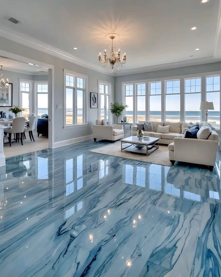 Bright living room with glossy blue marble floor, beige sofas, large windows, chandelier, and sea view.
