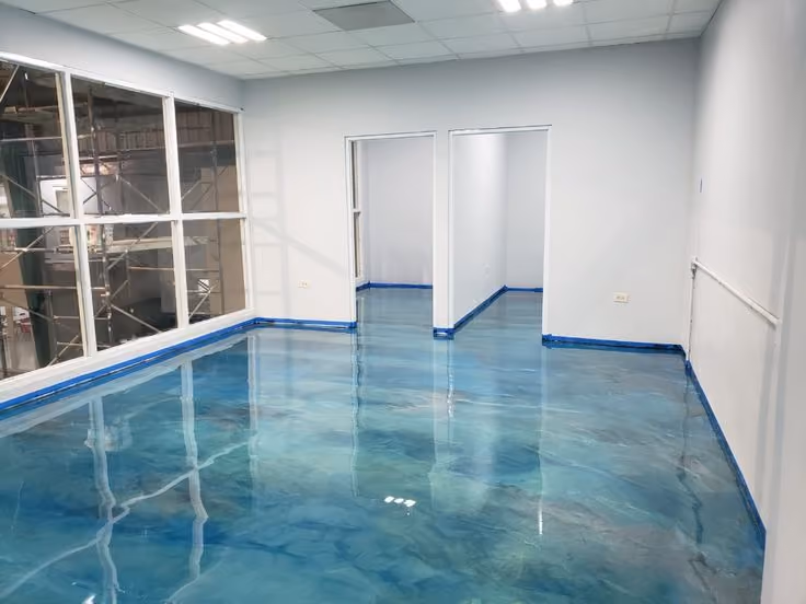 Empty room with glossy blue marbled epoxy floor reflecting ceiling lights and windows.