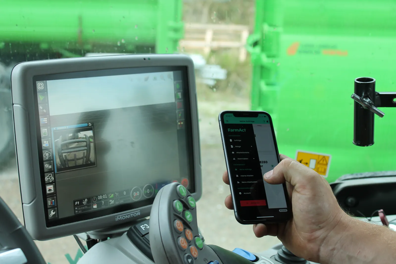 Blick in die Traktorkabine: Fahrer bedient die FarmAct App auf dem Smartphone