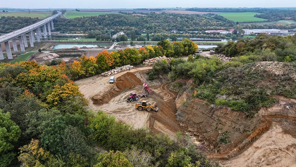 Erdbewegung auf einer Baustelle aus der Luft, im Hintergrund eine Brücke