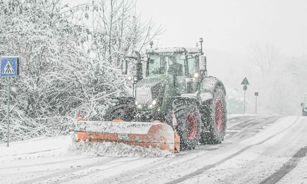Traktor mit Schneepflug beim Winterdienst auf verschneiter Straße