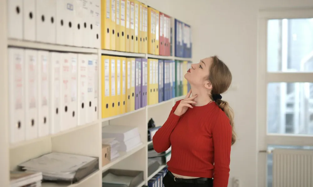Mitarbeiterin vor einem Regal voller Aktenordner im Büro