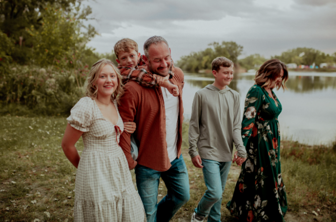Family of five walking by a lake holding hands and smiling on a cloudy day.