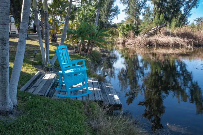 Blue rocking chair on a wooden dock overlooking a calm lake surrounded by trees.