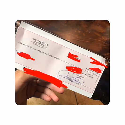 Hand holding a signed paper check with some details obscured in red.