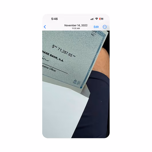 Photo of a check for $71,287.65 partially inside an envelope over a person's leg in shorts.
