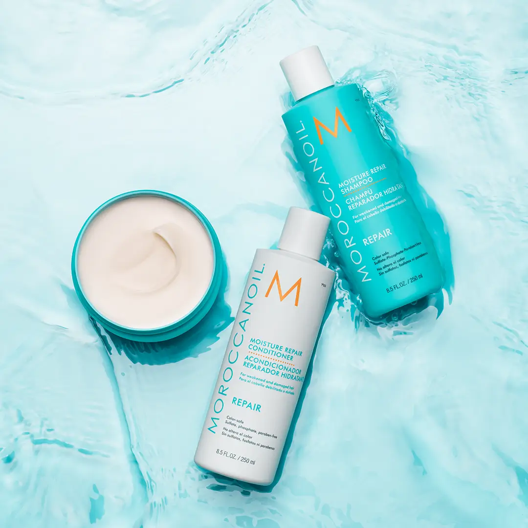 Moroccanoil moisture repair shampoo, conditioner, and cream on light blue water background.