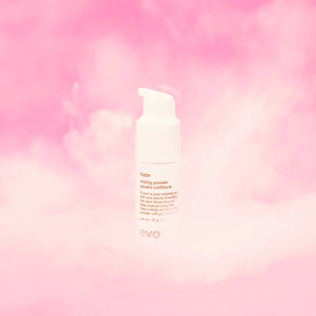 White pump bottle of Evo Haze styling powder with pink smoky background.