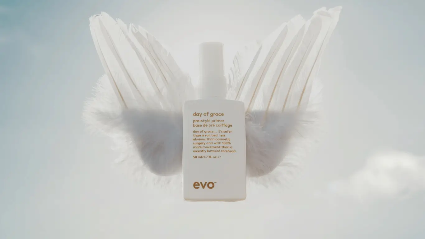 White bottle of Evo Day of Grace pre-style primer with angel wings and soft blue sky background.