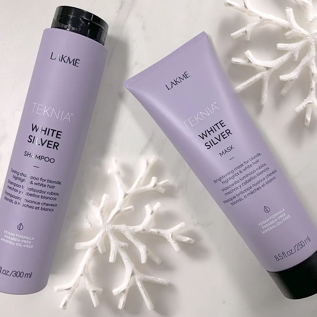 Two lavender Lakmé Teknia White Silver haircare products on white surface with white decorative snowflakes.