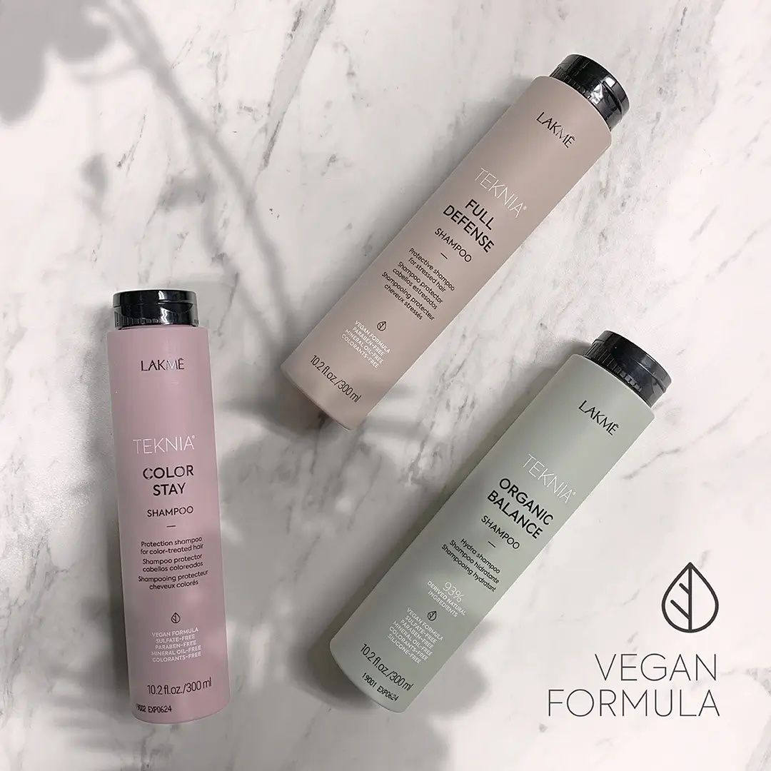 Three Lakmé Teknia shampoo bottles in pastel colors on marble with vegan formula text and leaf icon.