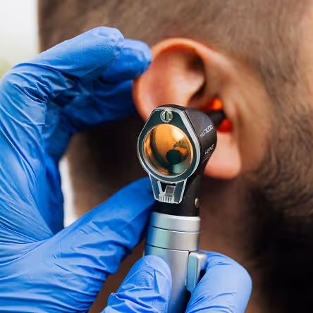 Doctor wearing blue gloves using an otoscope to examine a man's ear.