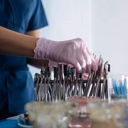 Gloved hand selecting dental tools from a metal organizer in a clinical setting.
