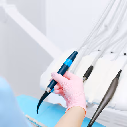 Hand with pink glove holding a blue dental tool near other dental instruments.
