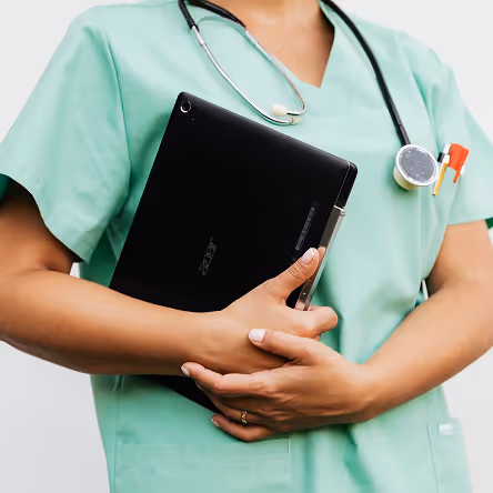 Healthcare worker in green scrubs holding a black Acer tablet with a stethoscope around the neck.