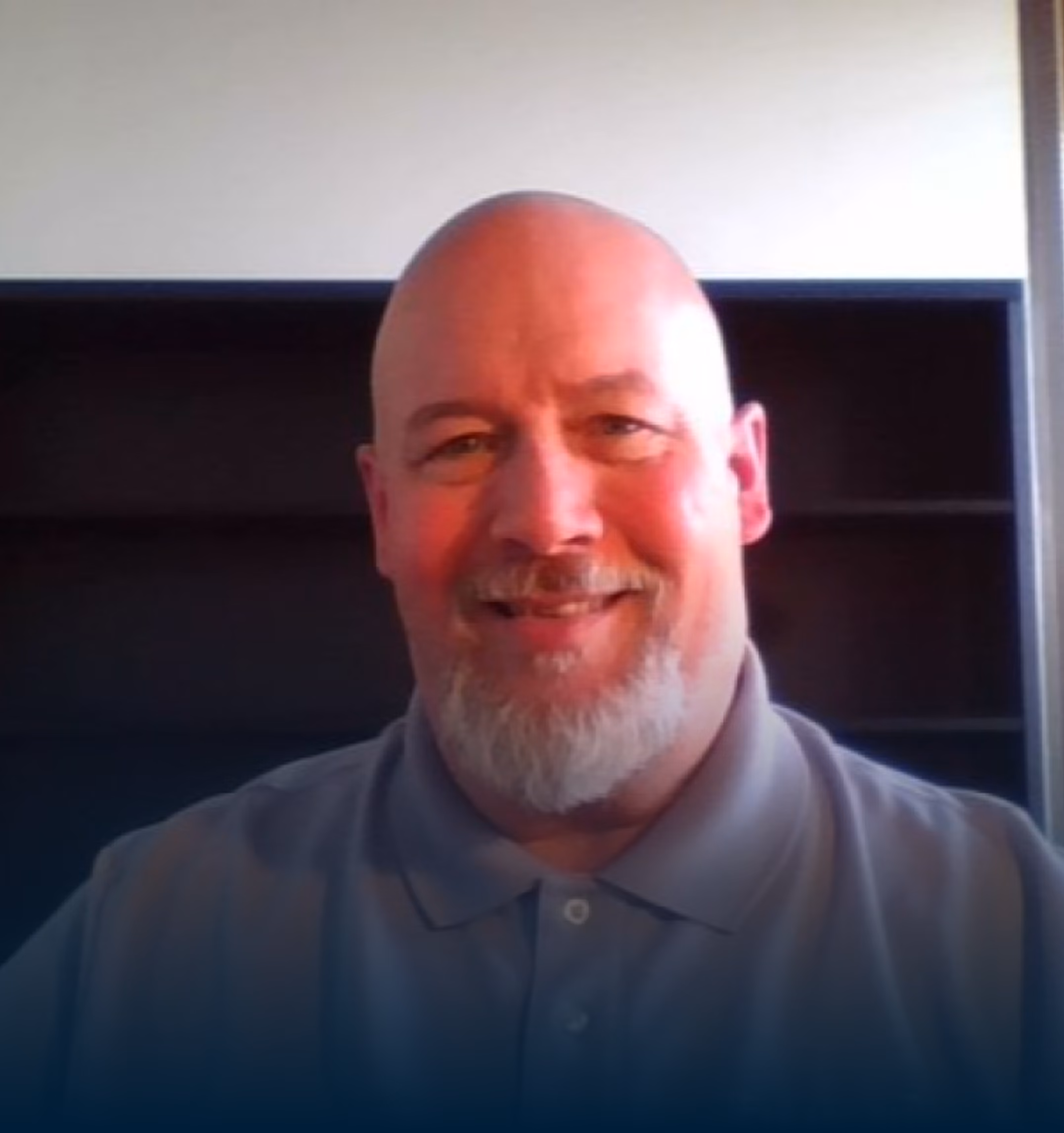 Smiling bearded man with short dark hair wearing a checked button-up shirt against a white background.