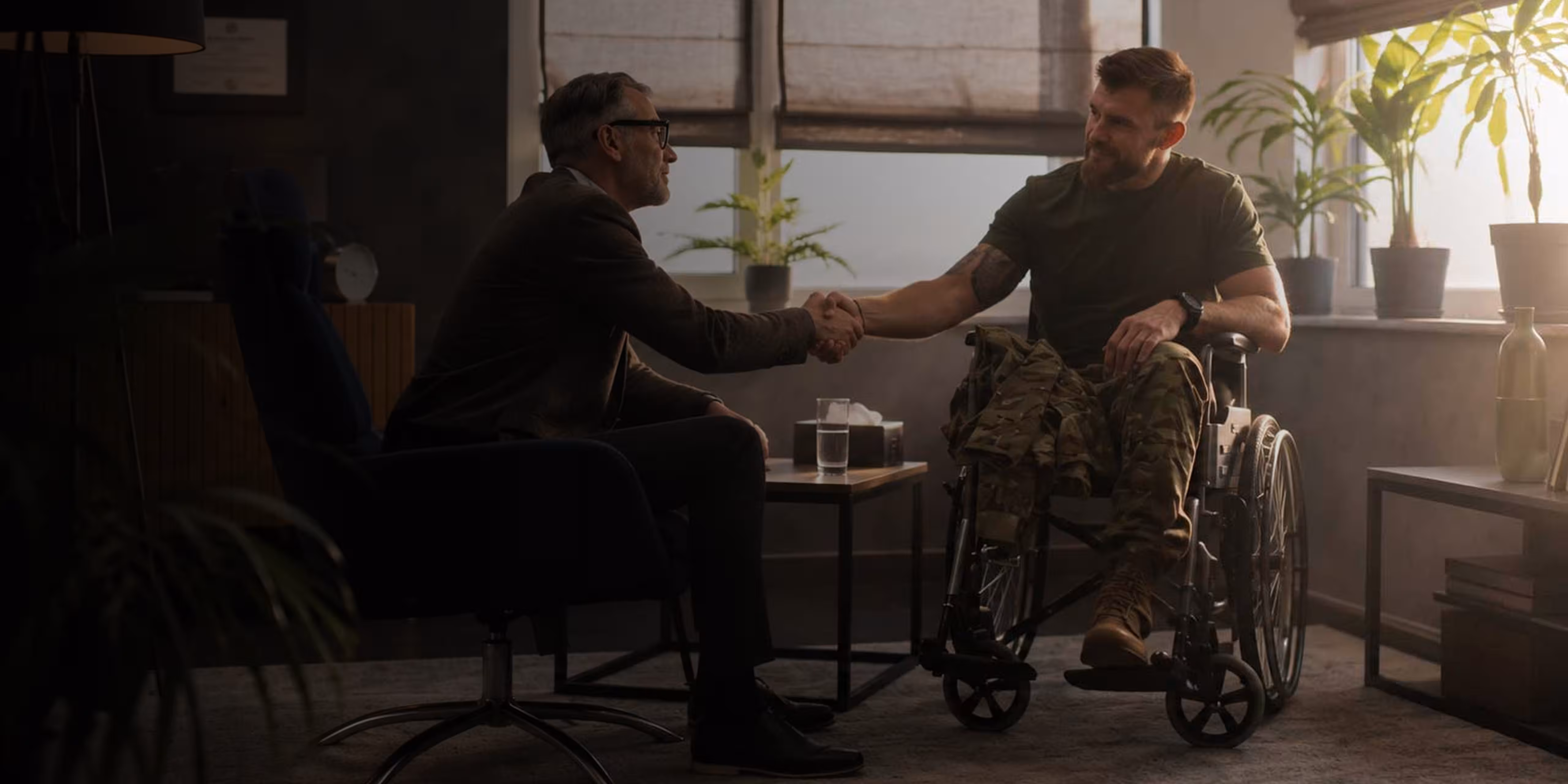 Man in military pants talks while seated with two women in a casual indoor setting.