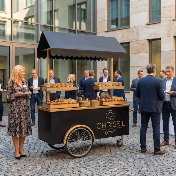 Menschen im Geschäftsbereich um einen Catering-Wagen mit Snacks und Getränken in einem Innenhof.