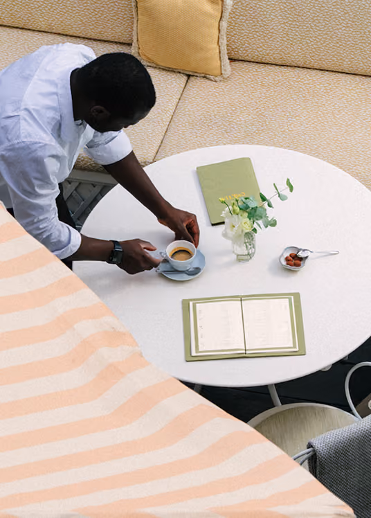 Serveur déposant un café sur une table ronde dressée avec menus verts et bouquet de fleurs sur une terrasse