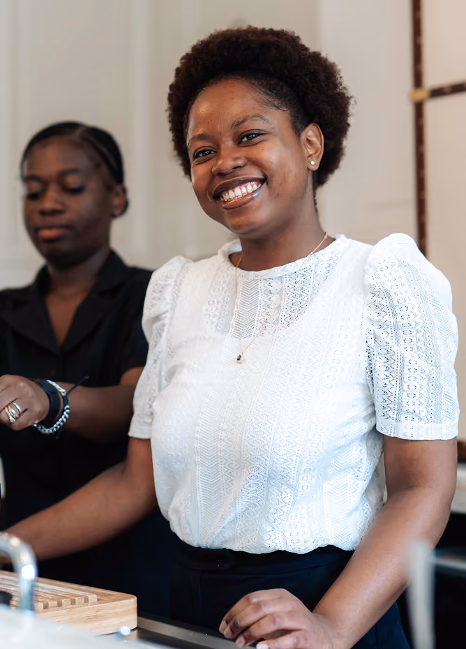Portrait souriant d'une femme en haut de dentelle blanche, avec une collègue en arrière-plan dans un intérieur clair