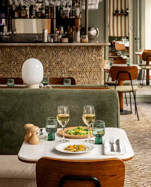 Table de restaurant dressée avec plats et verres à vin devant un bar au comptoir en mosaïque