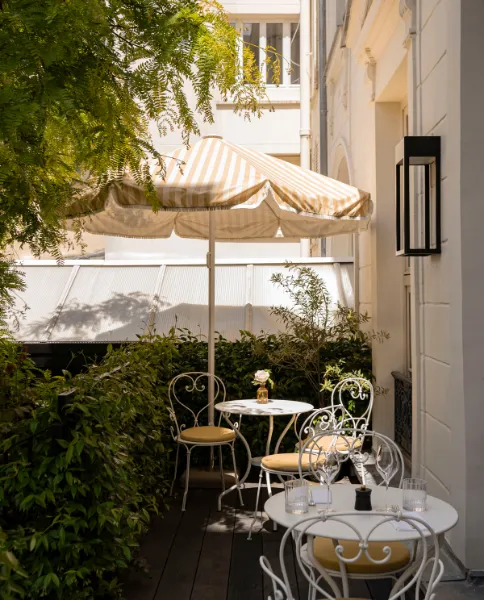 Terrasse ombragée avec chaises en fer forgé blanc, parasol rayé et végétation grimpante