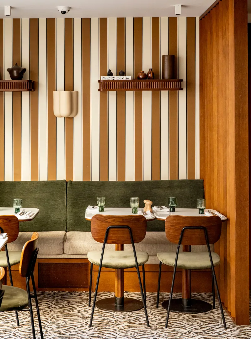 Restaurant interior with a bench and stools, a wall with gold stripes and a green velvet bench