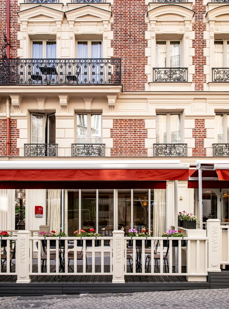 The stone façade of a Parisian building with wrought-iron balconies and a red awning on the ground floor