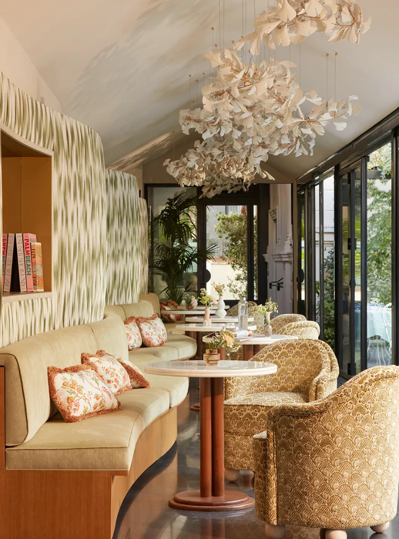 A bright living room with a curved beige bench, a floral chandelier and a bay window overlooking the garden