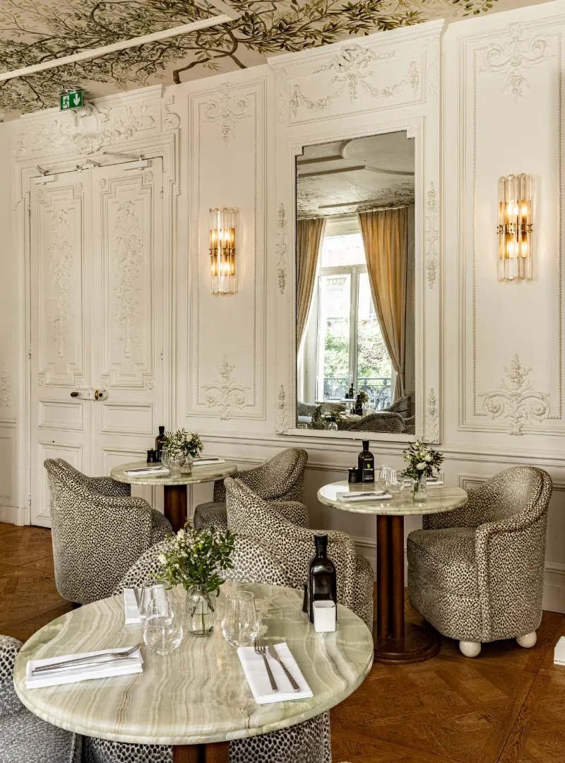 An elegant lounge with upholstered armchairs, round marble tables and a wall mirror set against panelling