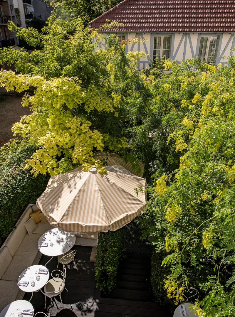 Aerial view of a tree-lined patio with a beige parasol, surrounded by lush greenery