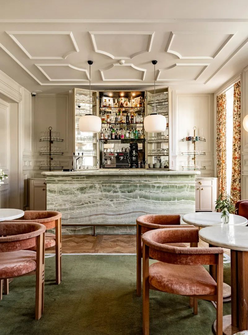 Bar avec plafond mouluré, fauteuils en cuir orange et étagères à bouteilles éclairées