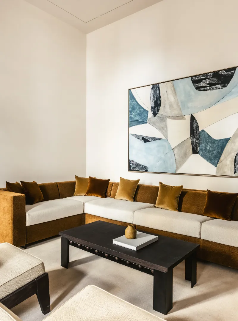 Living room with a white corner sofa and beige cushions, a black coffee table and an abstract painting on the wall