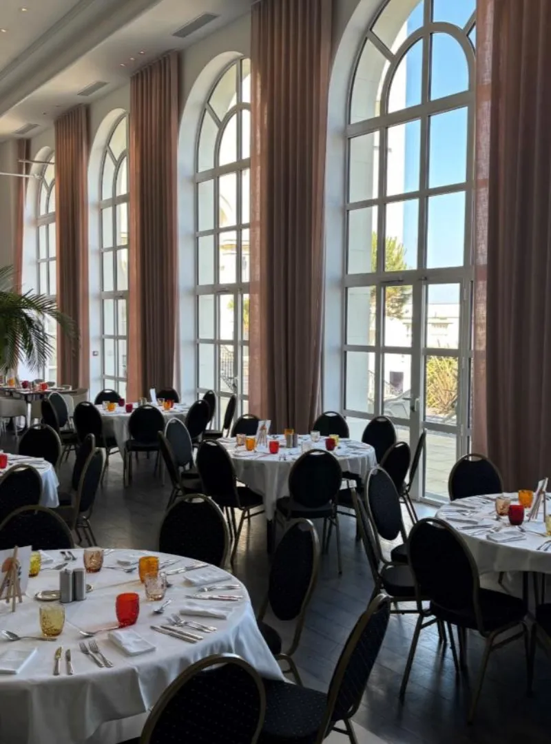 Salle de réception lumineuse avec grandes fenêtres arquées, tables dressées et chaises noires