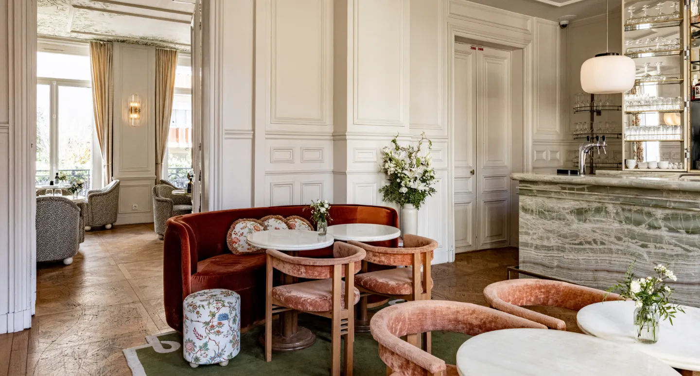 Salon boisé avec banquette rouille en velours, fauteuils roses et bar en marbre veiné vert