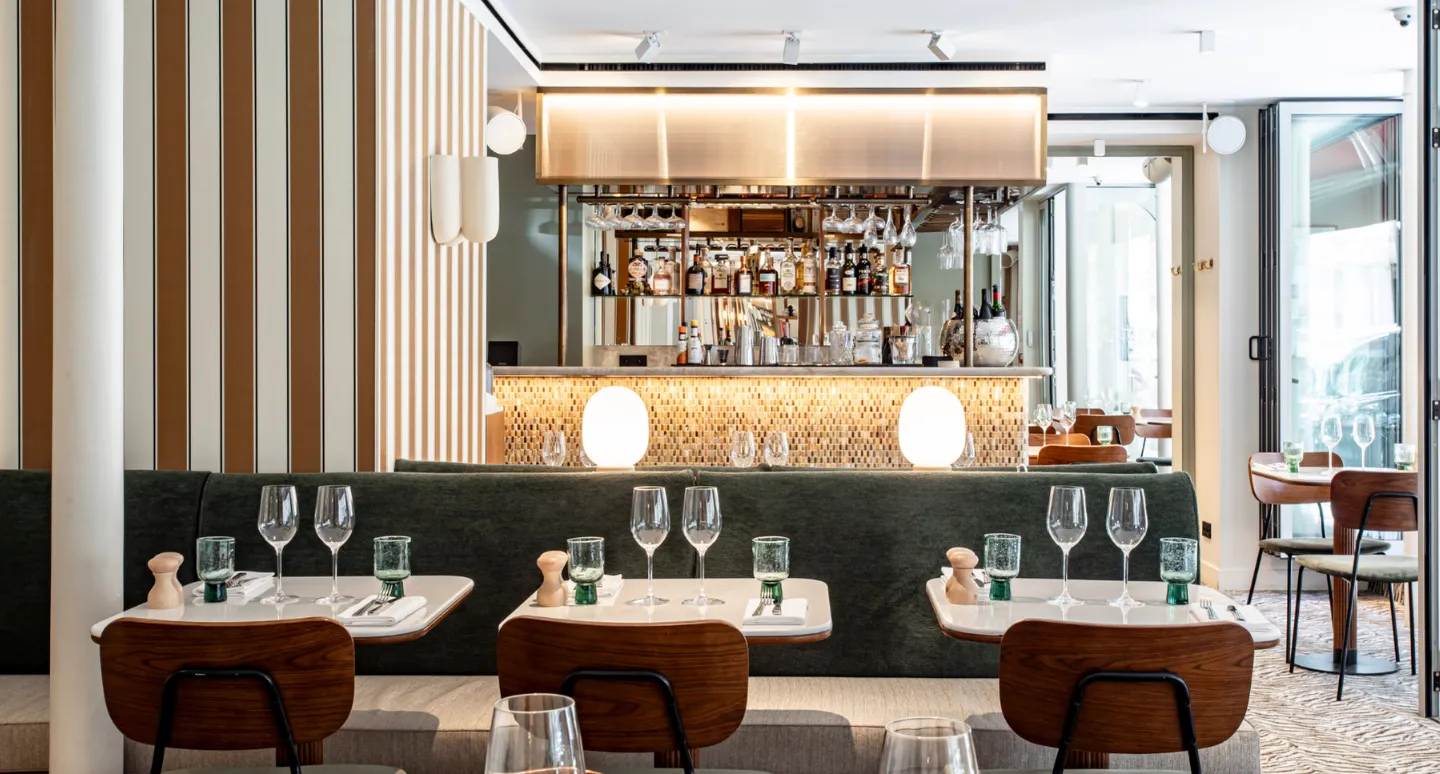 Restaurant moderne avec banquette verte, tables dressées de verres à vin et bar rétroéclairé en arrière-plan