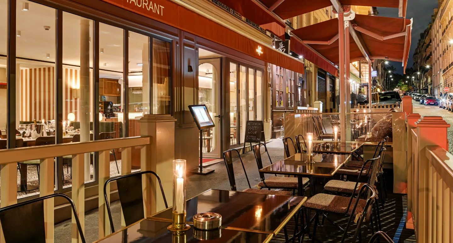 Terrasse de restaurant parisien de nuit, tables aux chandelles sous un auvent rouge en bordure de rue