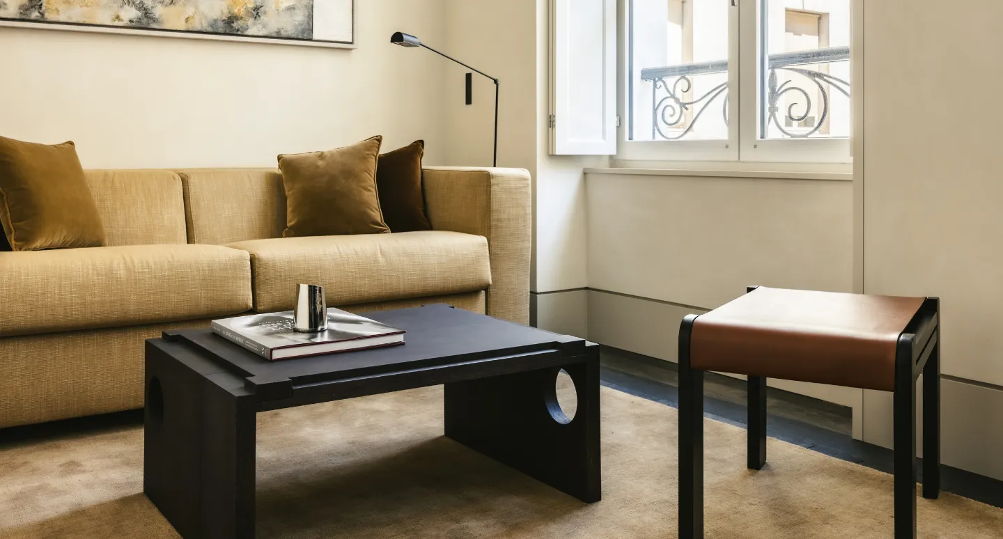 Salon avec canapé moutarde, table basse noire ajourée et tabouret en cuir marron, fenêtre à balcon parisien