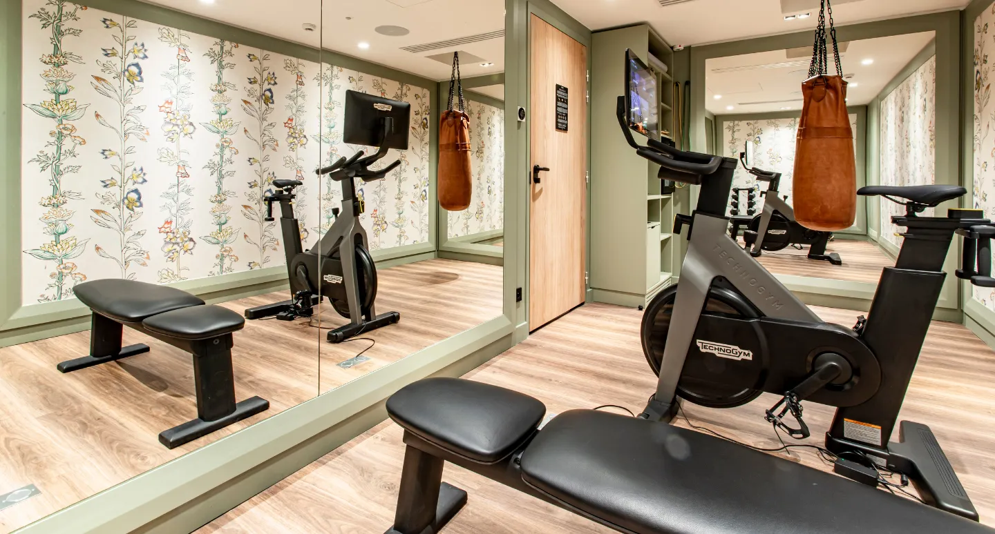 Salle de fitness avec vélo Technogym, banc de musculation et sac de frappe, murs à motifs floraux