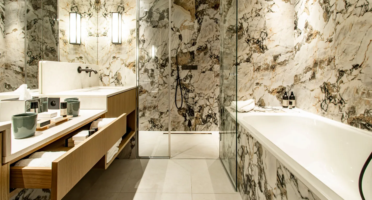 Salle de bain habillée de marbre veiné doré avec vasque en bois, douche vitrée et baignoire encastrée