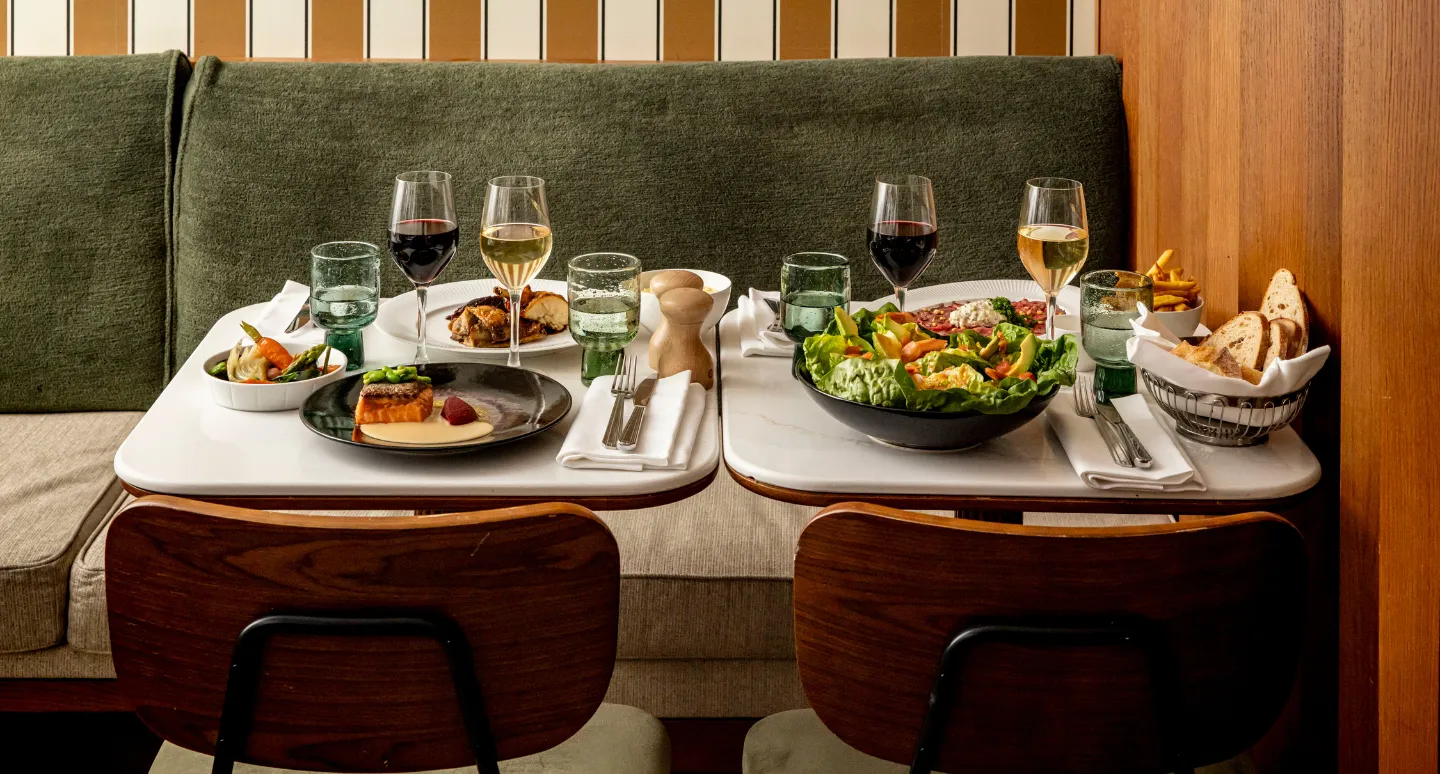 Deux tables dressées avec saumon, salade composée et charcuterie, accompagnées de verres de vin sur banquette verte
