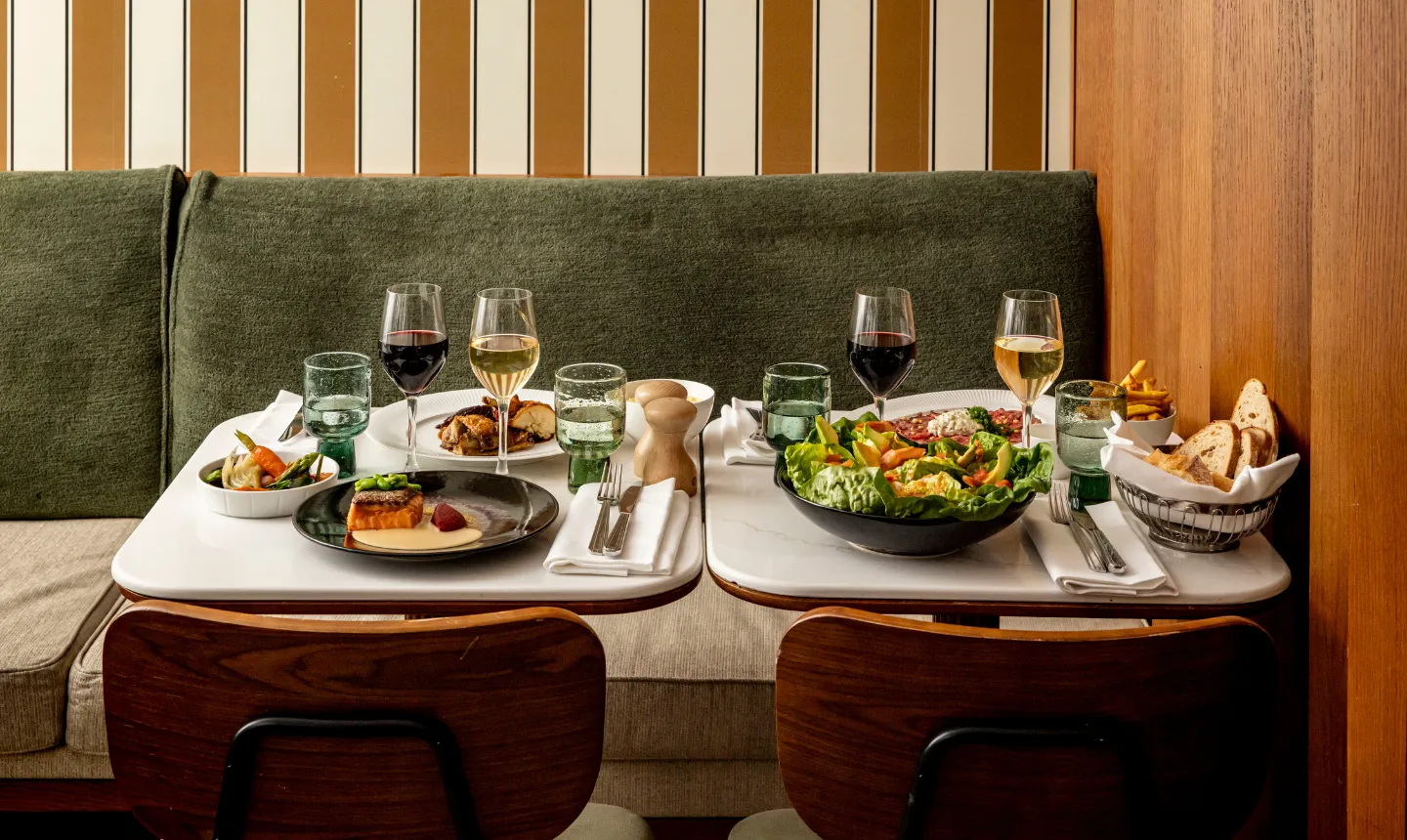 Deux tables de restaurant dressées avec plats de saumon, salade et charcuterie accompagnés de verres de vin