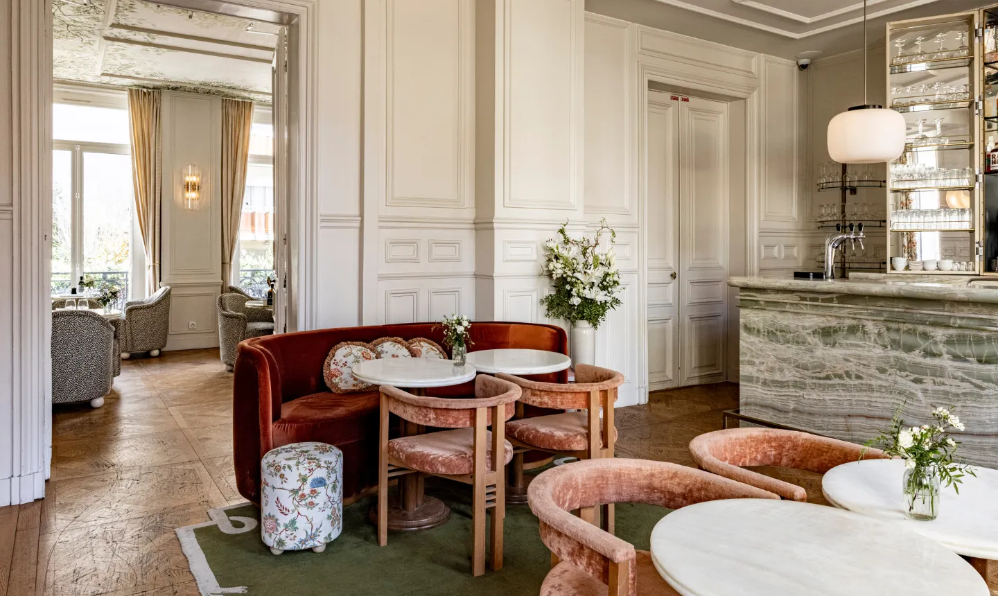 Bar élégant aux boiseries blanches avec banquette rouille, fauteuils roses et comptoir en marbre veiné