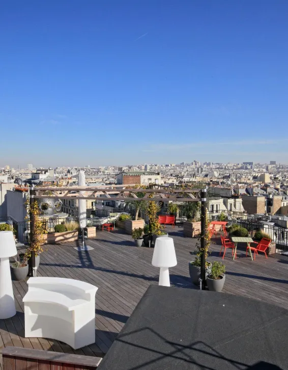 Vue panoramique d'un rooftop parisien avec canapés blancs et jardinières fleuries, toits de la ville en arrière-plan