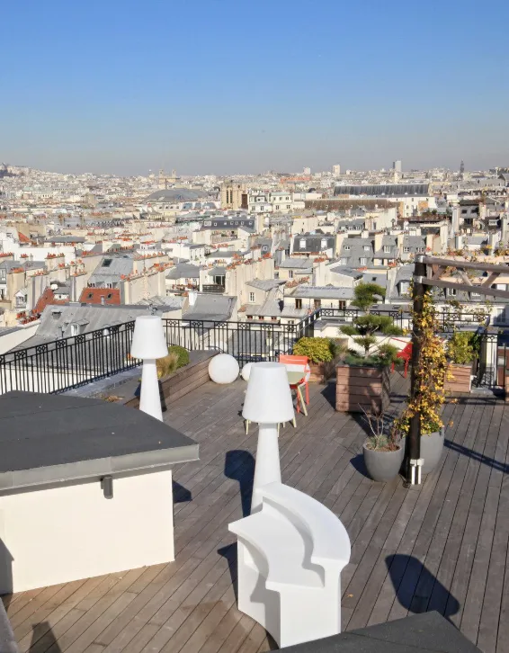 Vue sur les toits de Paris depuis un rooftop avec cheminées et transats blancs