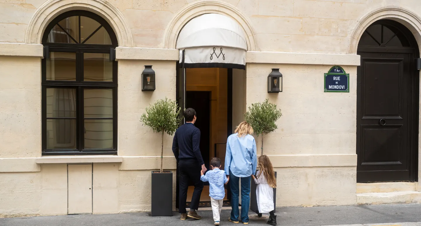 Famille entrant dans l'hôtel Mondovi, façade en pierre ornée d'oliviers, plaque de la rue de Mondovi