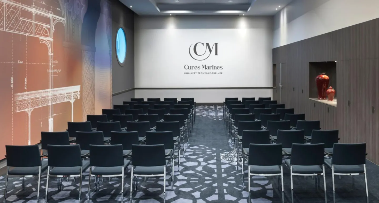 Salle de conférence disposée en rangées de chaises noires, avec écran affichant le logo Cures Marines MGallery