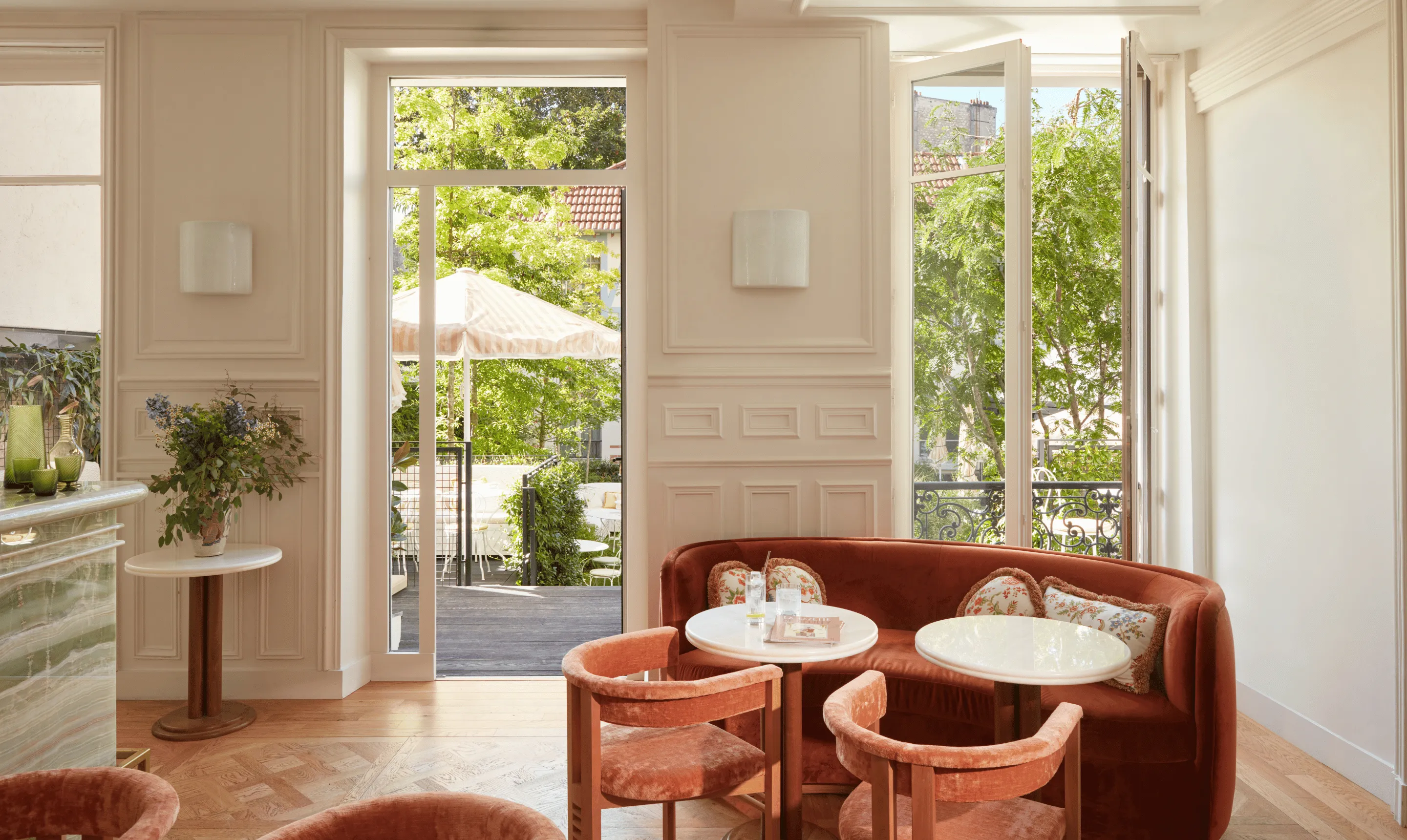 Salon avec canapé et fauteuils beiges devant une grande fenêtre donnant sur un jardin verdoyant